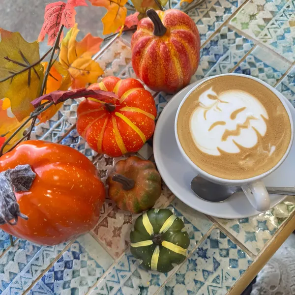 Pumpkin latte art surrounded by autumn leaves and mini pumpkins
