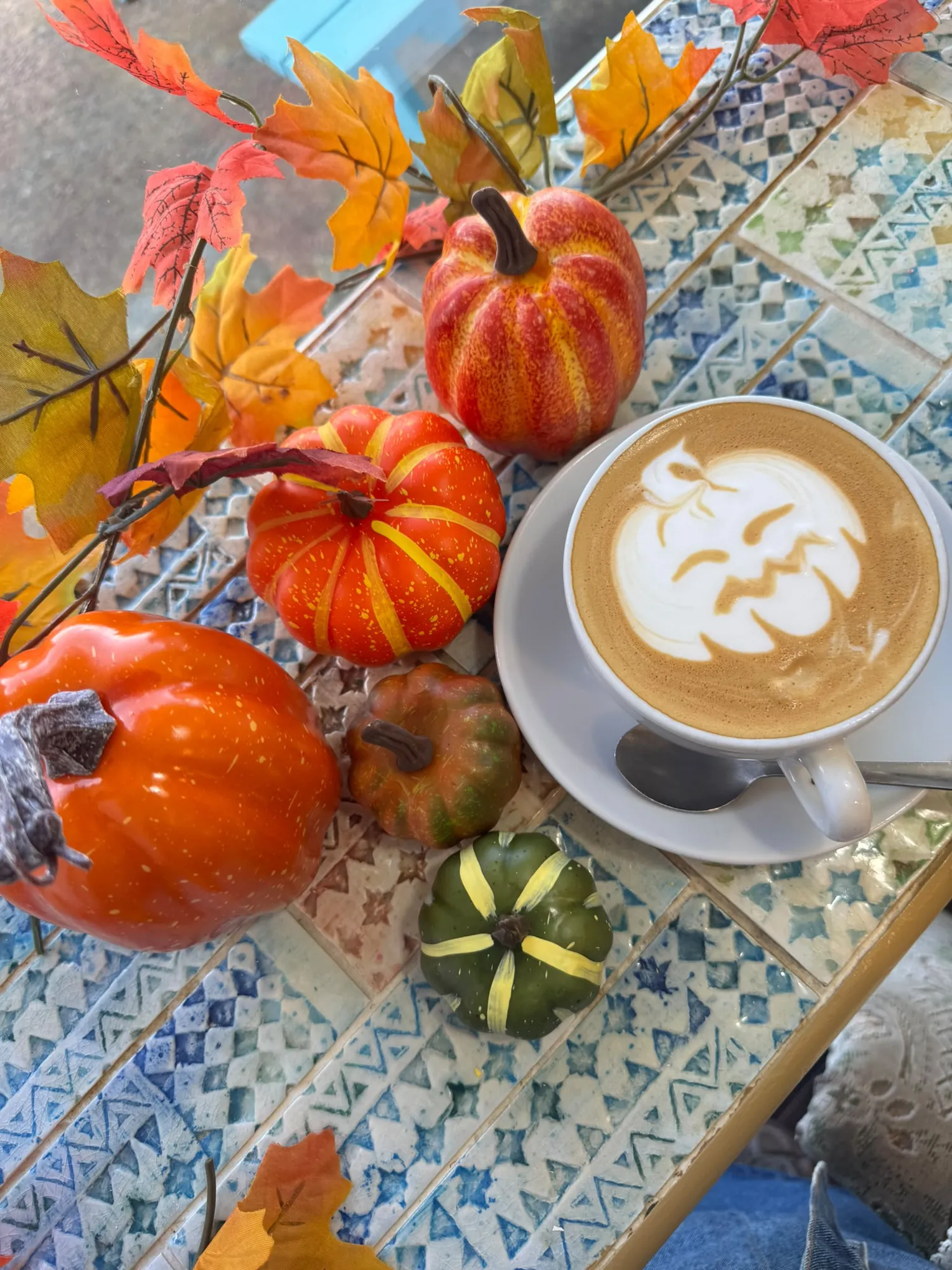 Latte with pumpkin latte art, surrounded by autumn leaves and mini pumpkins