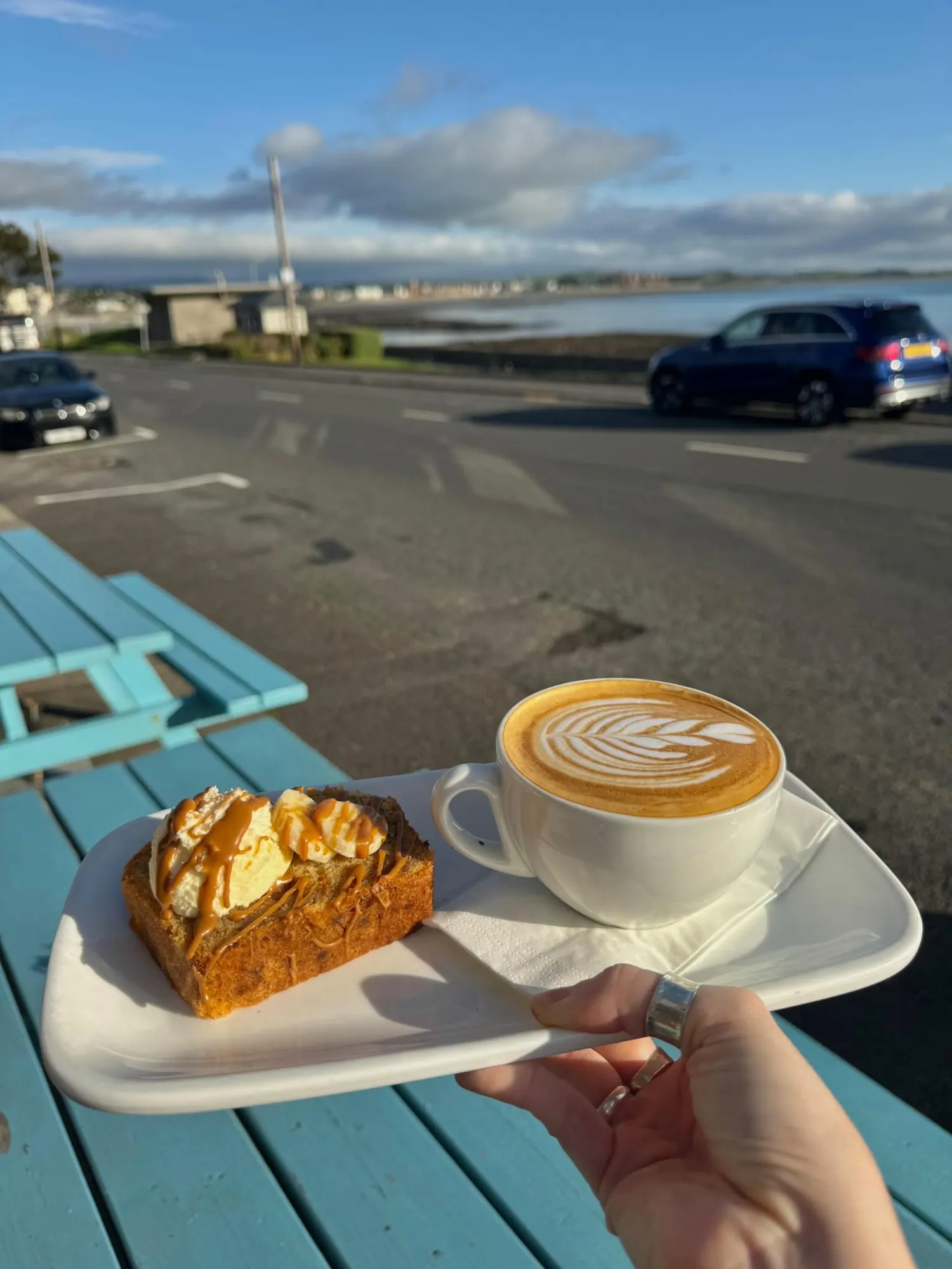 Biscoff banana bread and a cappuccino on a picnic table on the promenade