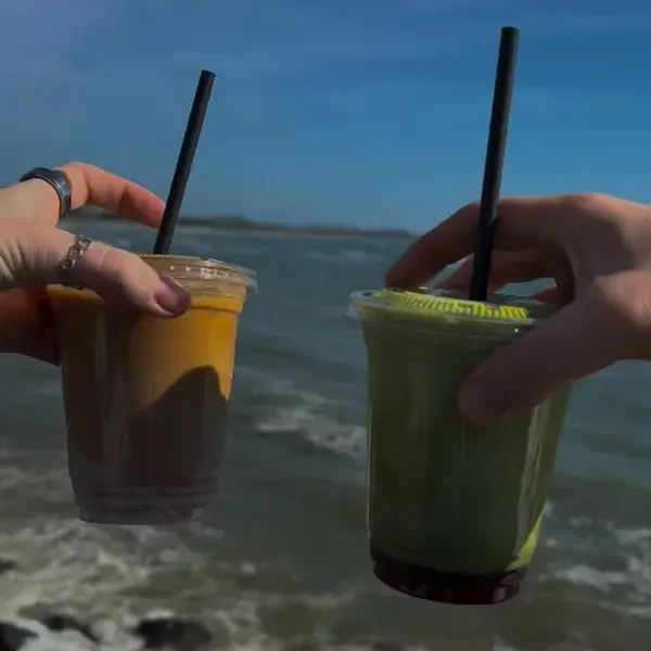 Iced coffee and iced strawberry matcha held up over the sea